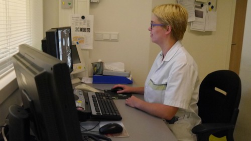 De laborant zit achter een ruit en bedient de CT-scan
